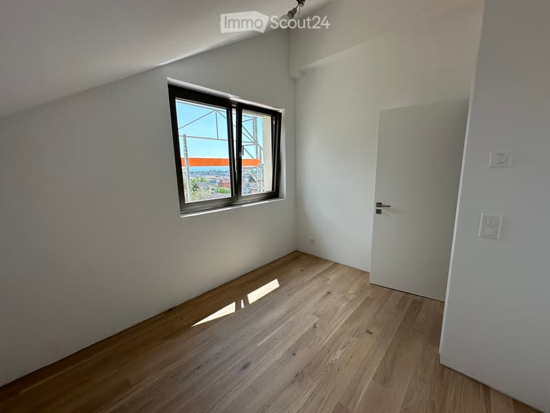 Empty room with wooden flooring, white walls, and a large window offering a view of the cityscape.