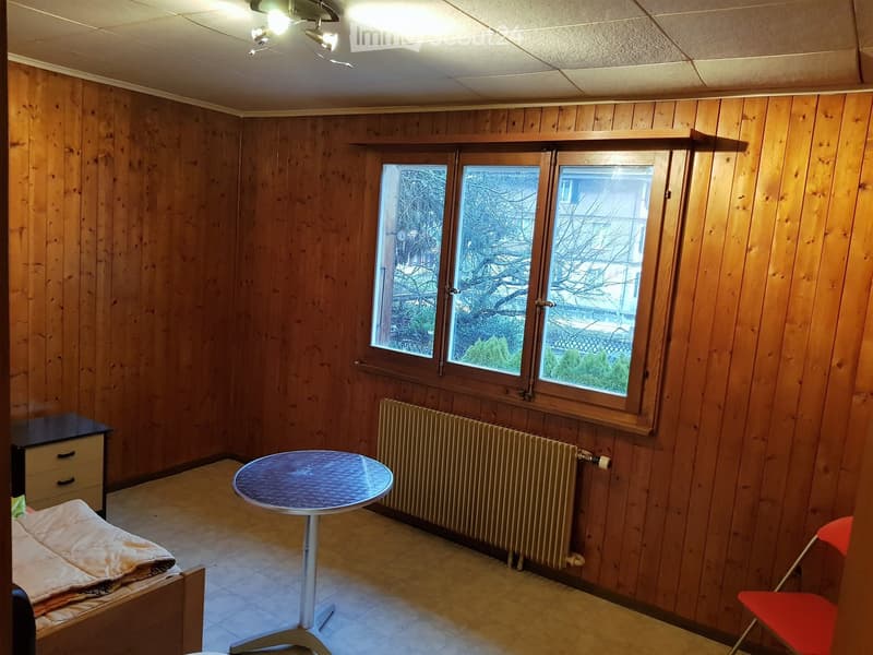 Wooden walls, a radiator, a table, a bed, a chair, drawers, a window with view