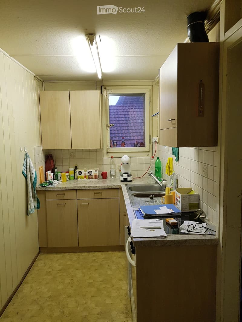 Wooden cabinets, countertop, sink, kettle, bottles, window