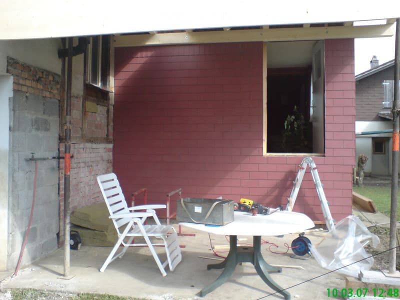 Red brick building, construction work ongoing, tools on table, white chair, open window
