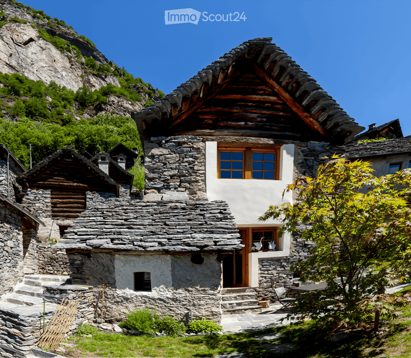 Stone house with wooden doors and windows, situated in a mountainous area with a stone staircase leading to the entrance.