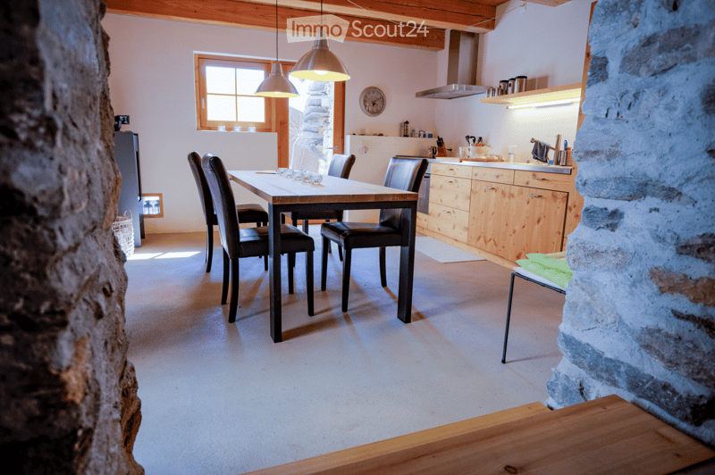 Open-plan dining and kitchen area with wooden cabinets, a dining table with chairs, pendant lights, and a clock on the wall.