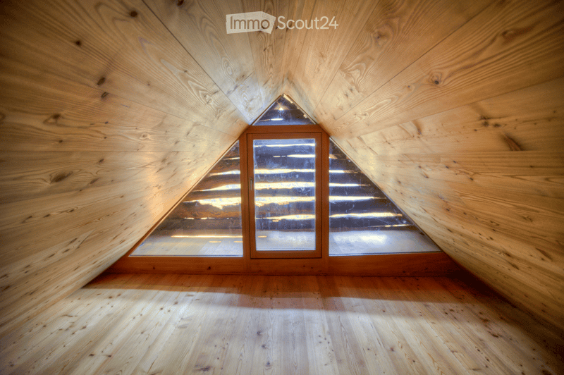 An empty attic space with wooden walls and floor, featuring a large skylight window and a sliding glass door leading to another room.