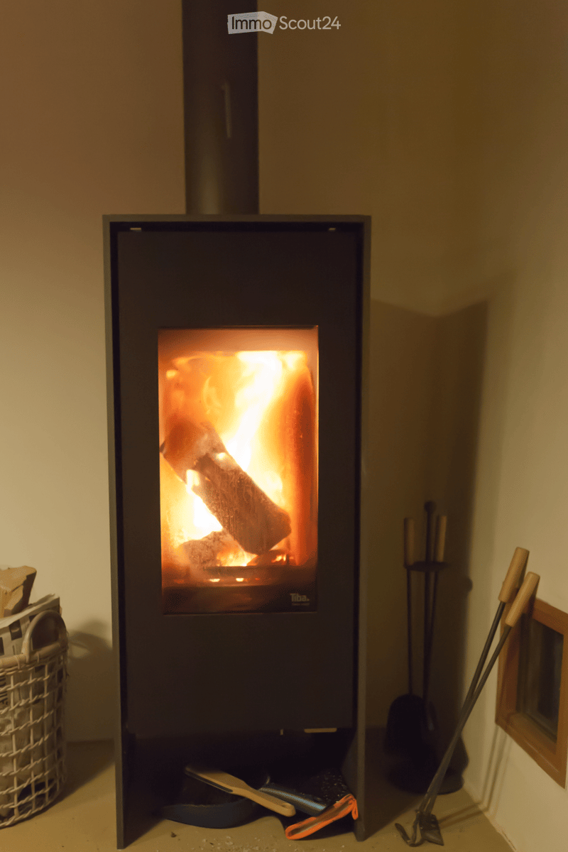 A modern wood-burning fireplace with a glowing fire, surrounded by fireplace tools and a woven basket on the floor.