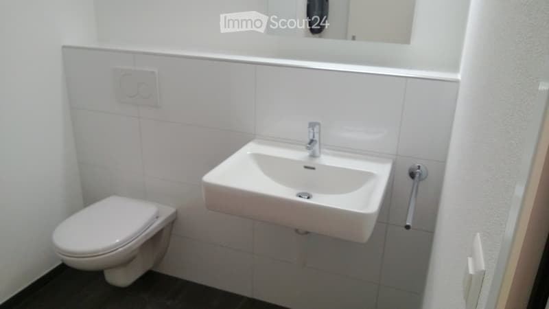 Modern bathroom with white tiled walls, a toilet, a sink with a modern faucet, and a mirror above the sink.