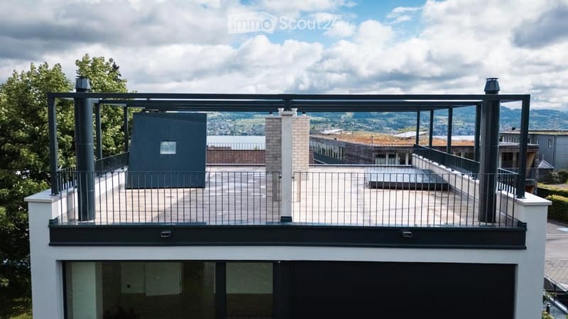 Modern rooftop terrace with metal railings, a small structure, and a scenic view of the surrounding landscape and water.