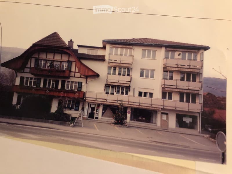 Multi-story building with balconies, large windows, and a mix of architectural styles including a traditional section with a pitched roof and a modern section with flat balconies.