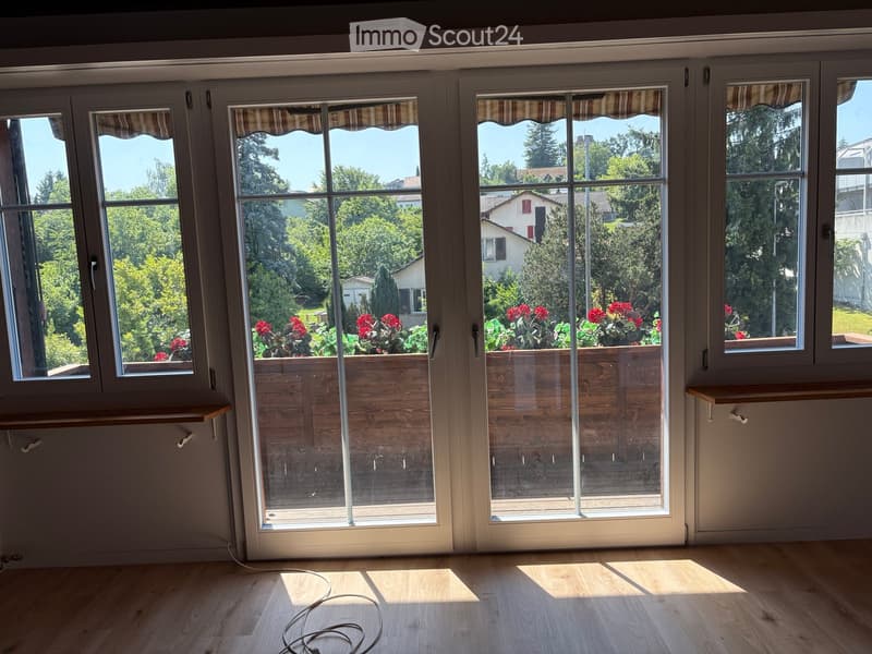 Empty room with wooden flooring, large sliding glass doors leading to a garden, and built-in shelves on either side of the doors.
