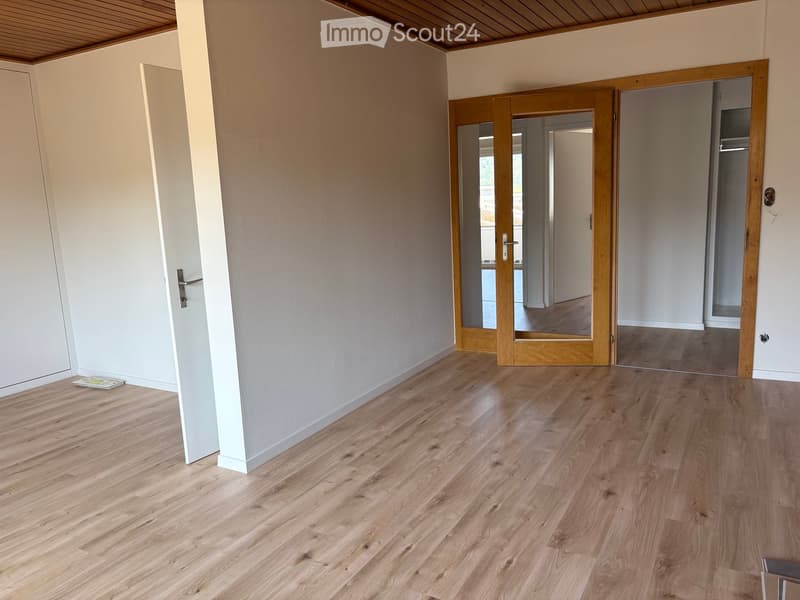Empty room with light wooden flooring, white walls, and a wooden door leading to another room.
