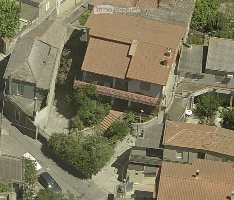 Aerial view of a multi-story residential building with a red-tiled roof, surrounded by neighboring structures and greenery.