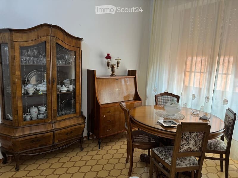Dining room with a round wooden table, six chairs, a large wooden cabinet with glass doors, and decorative items on the table and cabinet.