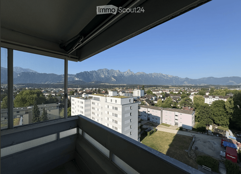 Balcony with a view of a cityscape, buildings, and distant mountains under a clear blue sky.