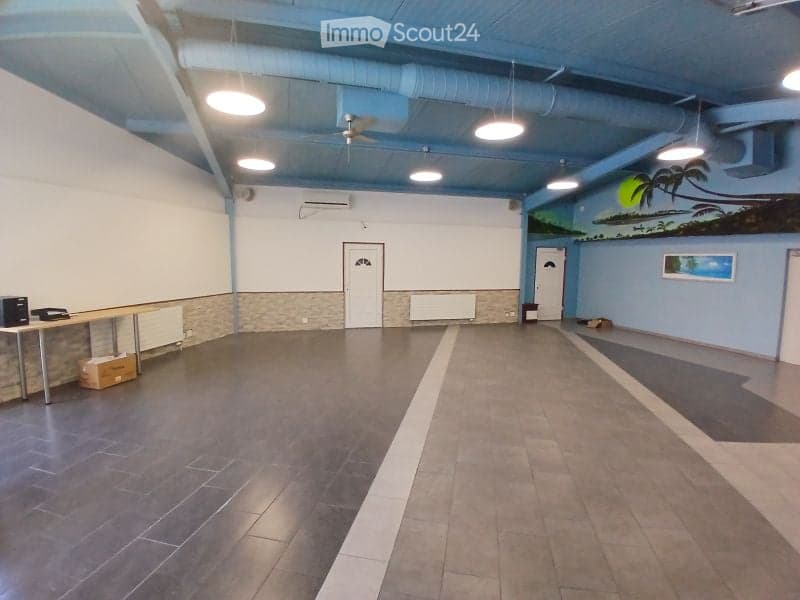 Empty room with tiled floor, white walls, and minimal furnishings including a small table and a few boxes. The room has a large mural on one wall and a ceiling fan with lights.