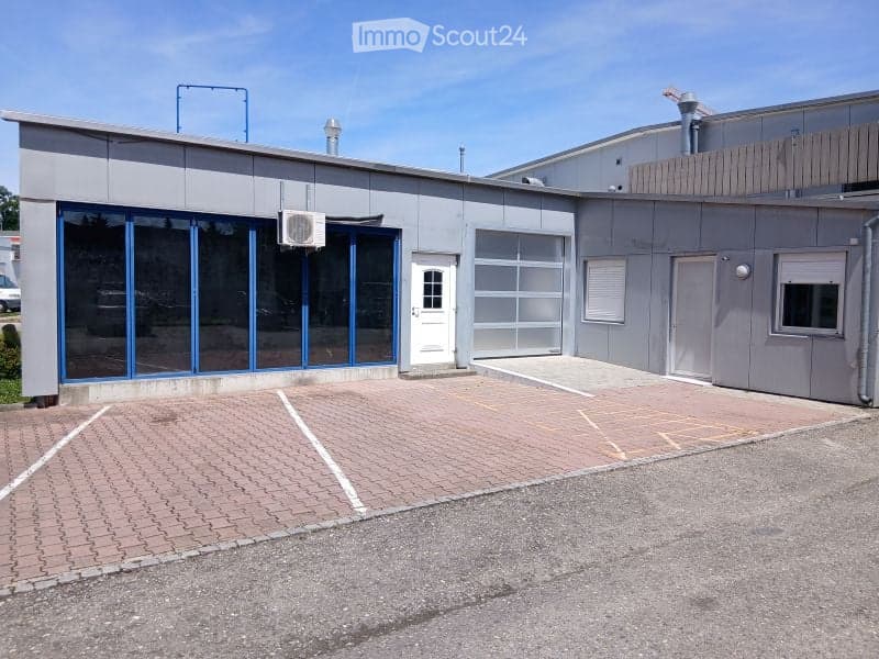 Modern industrial-style building with a flat roof, large garage door, and glass front entrance.