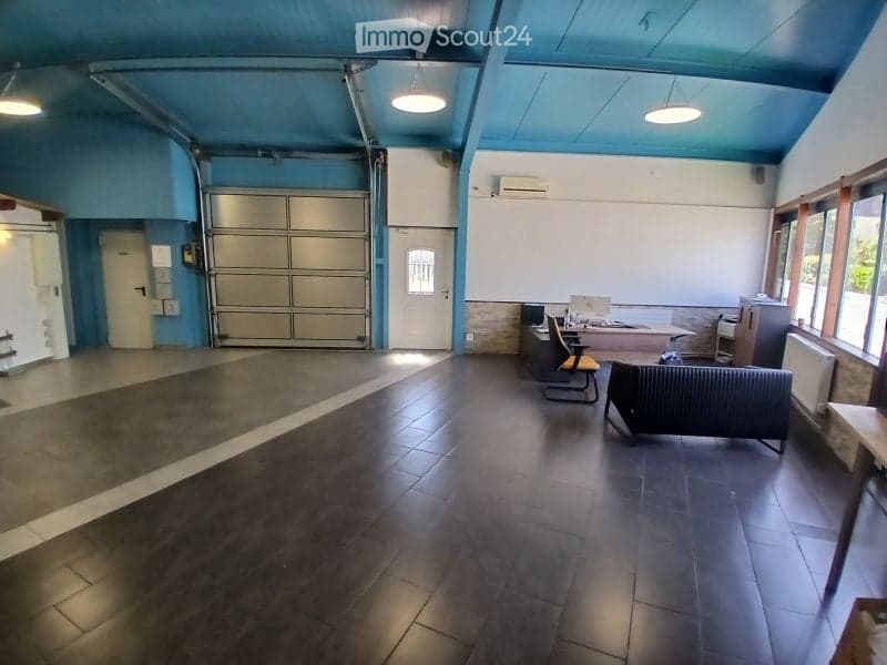 Spacious room with dark wooden flooring, blue ceiling, and large garage door. Contains a sofa, a chair, a small table with a laptop, and a few other items.