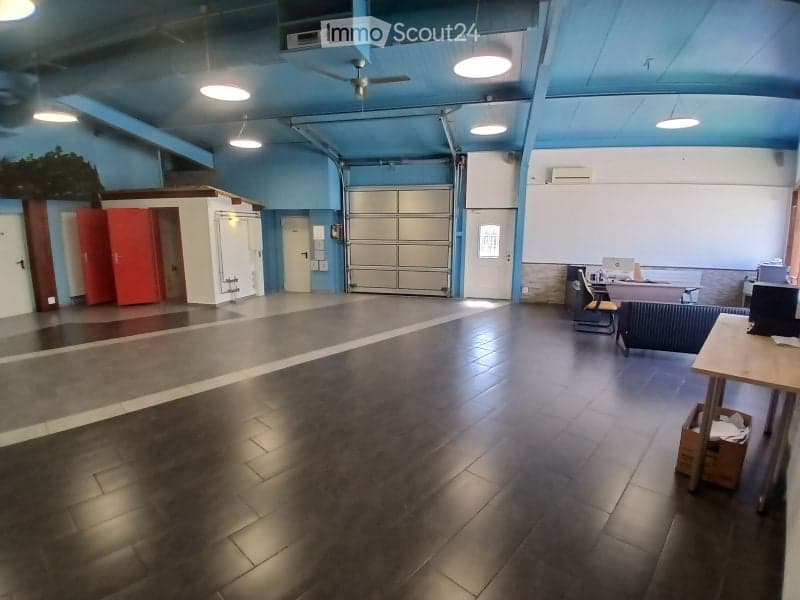 Spacious room with a dark tiled floor, blue walls, and a large garage door. Visible objects include a chair, a table with a laptop, and a refrigerator.