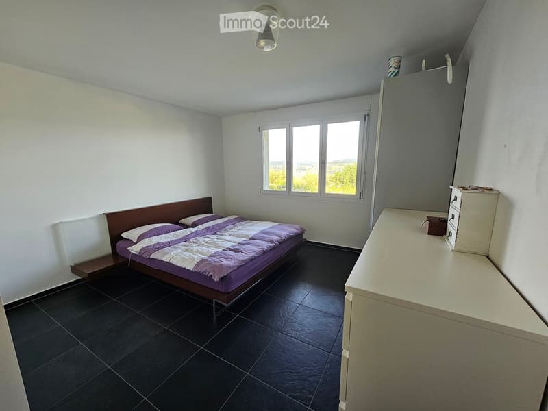 Bedroom with a double bed, nightstand, dresser, and mirror. The room features dark tiled flooring and large windows with a scenic view.