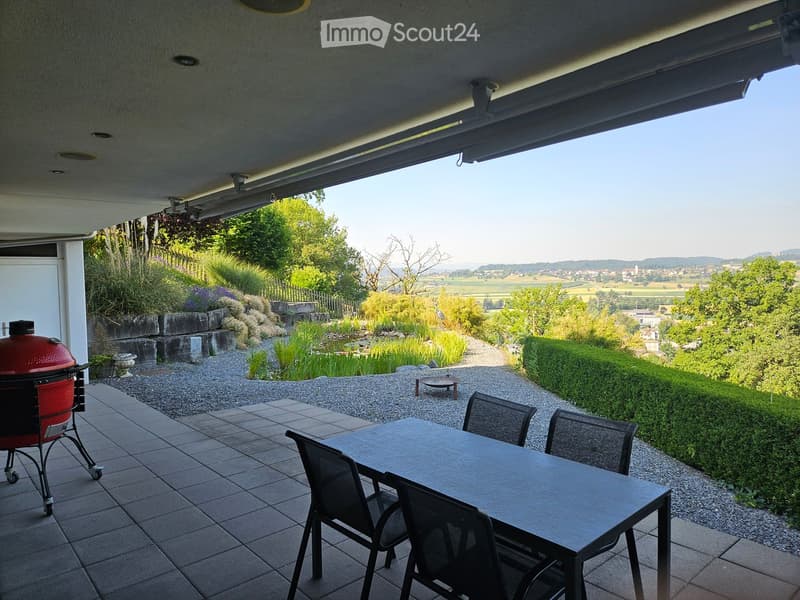 Outdoor patio with tiled floor, table and chairs, grill, and scenic view of greenery and countryside.