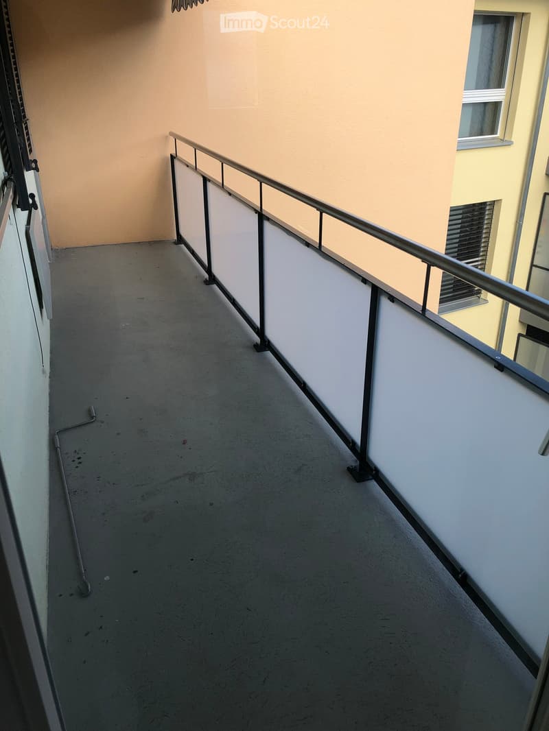 Balcony with white railing and flooring, beige walls, and an empty space with a door leading to another room