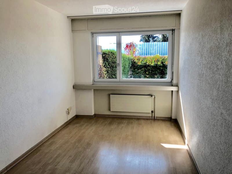 Empty room with wooden flooring, white walls, and a large window with a radiator below it.