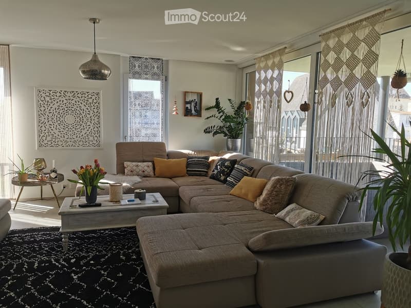 Modern living room with a large sectional sofa, coffee table, side table, pendant light, wall art, and plants.