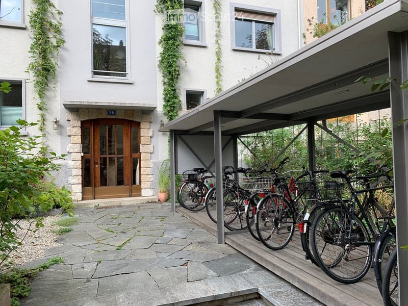 Two-story building with a covered bike parking area, several bicycles parked under the shelter, and a stone-paved entrance area.