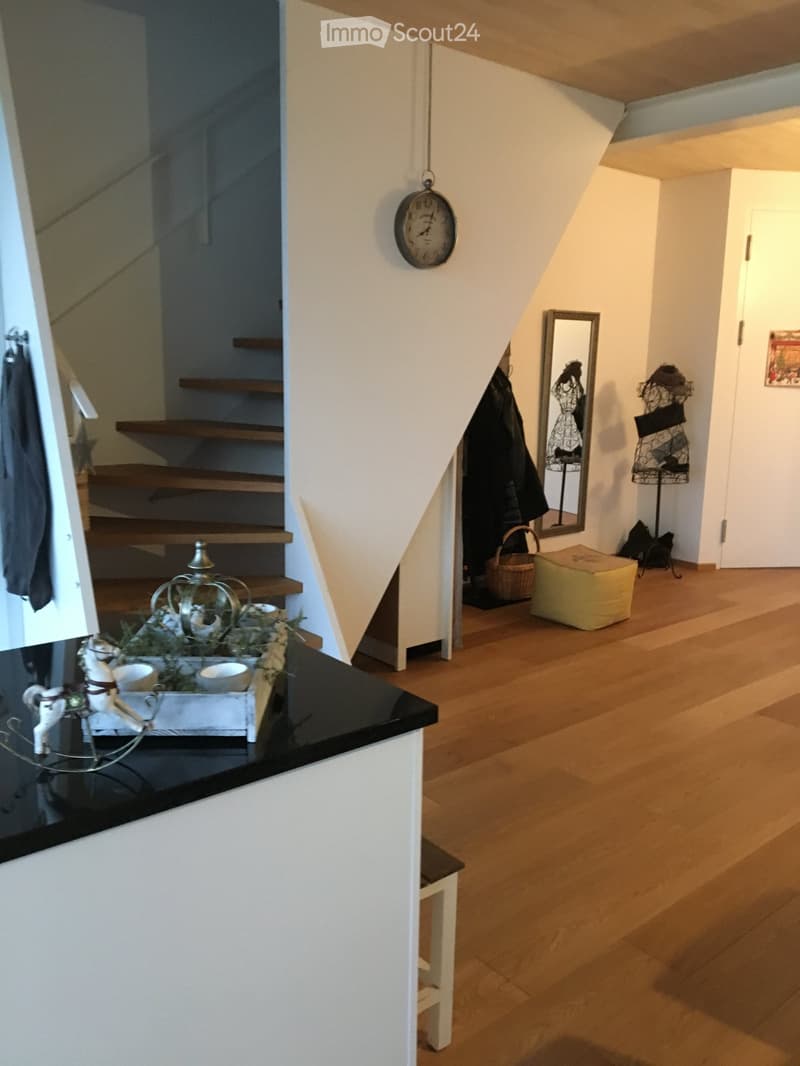 Spacious hallway with wooden flooring, staircase leading upwards, decorative items including a clock, mirror, coat rack, and small table with a toy horse and teapot set.