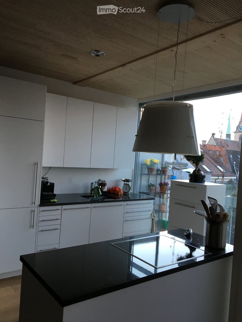 Modern kitchen with white cabinets, black countertop, induction stove, and various appliances. Features a large window with a view of the city.