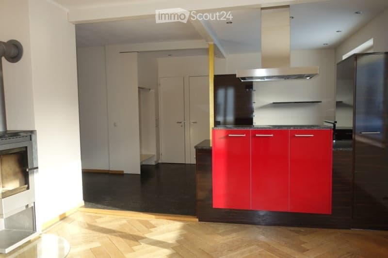 Modern kitchen with red cabinets, a central island, gas stove with an extractor hood, refrigerator, and a fireplace on the left.