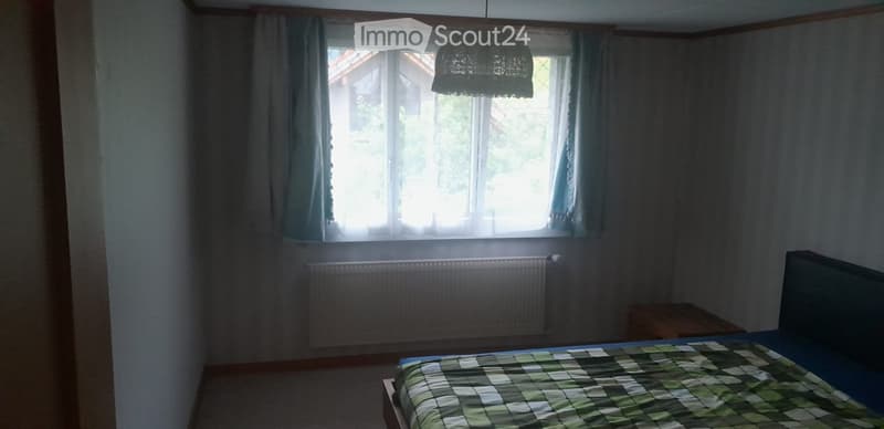 Bedroom with a bed, radiator, nightstand, and large window with curtains.