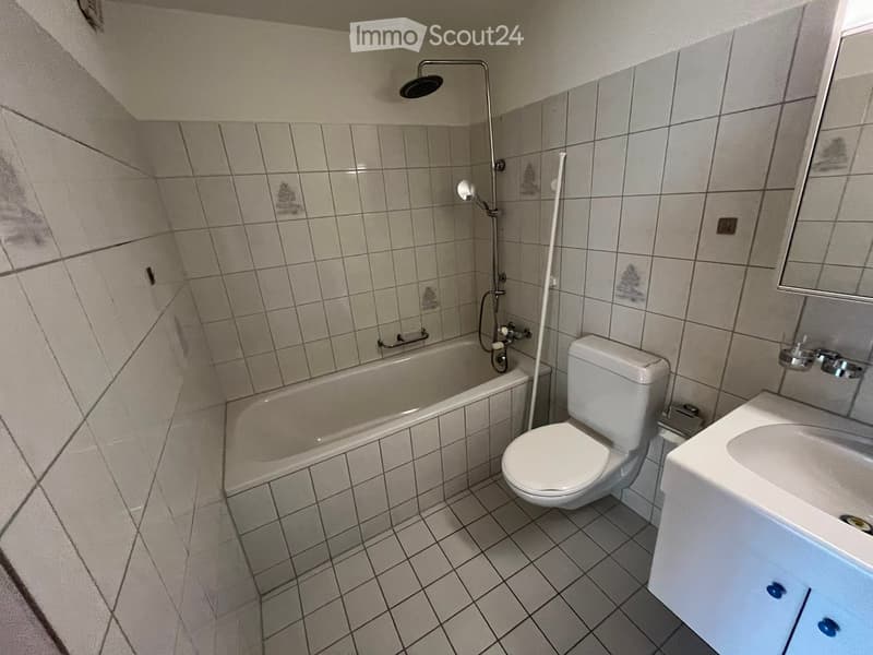 Bathroom with tiled walls and floor, featuring a bathtub, toilet, sink, and mirror. Showerhead and faucet are visible.