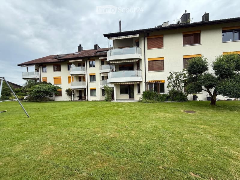 A multi-story residential building with balconies, large windows, and a well-maintained lawn in front.