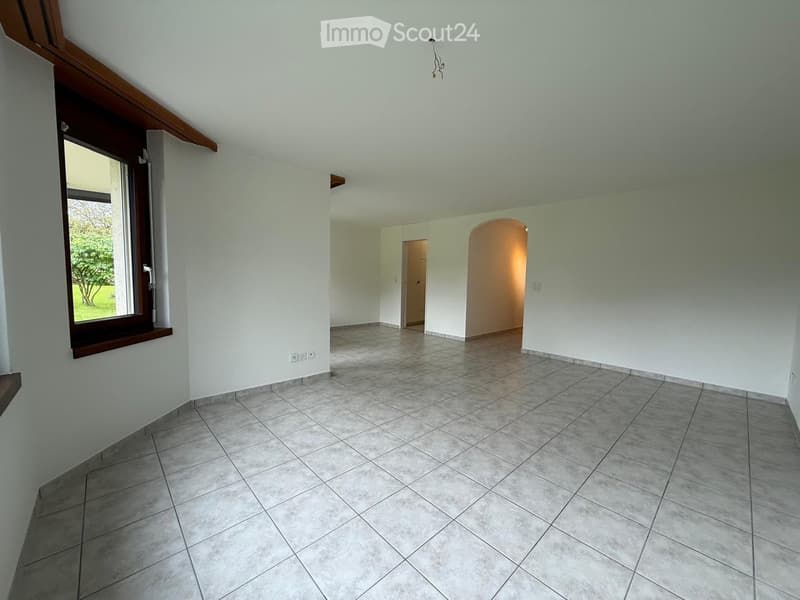 Empty room with tiled floor, white walls, large window with wooden frame, and two doors leading to other spaces.