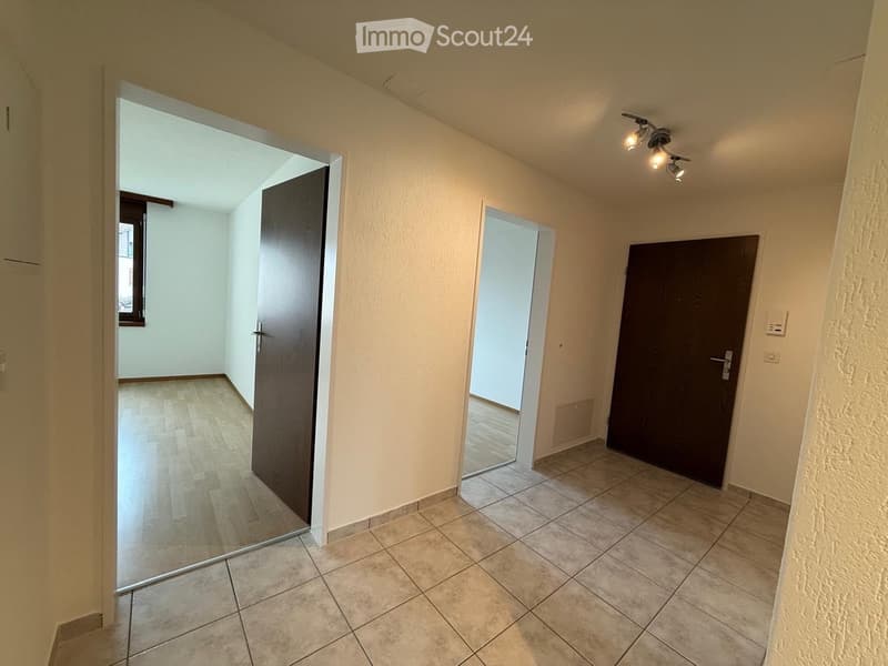 Empty hallway with tiled floor, wooden doors, and a small window at the end.