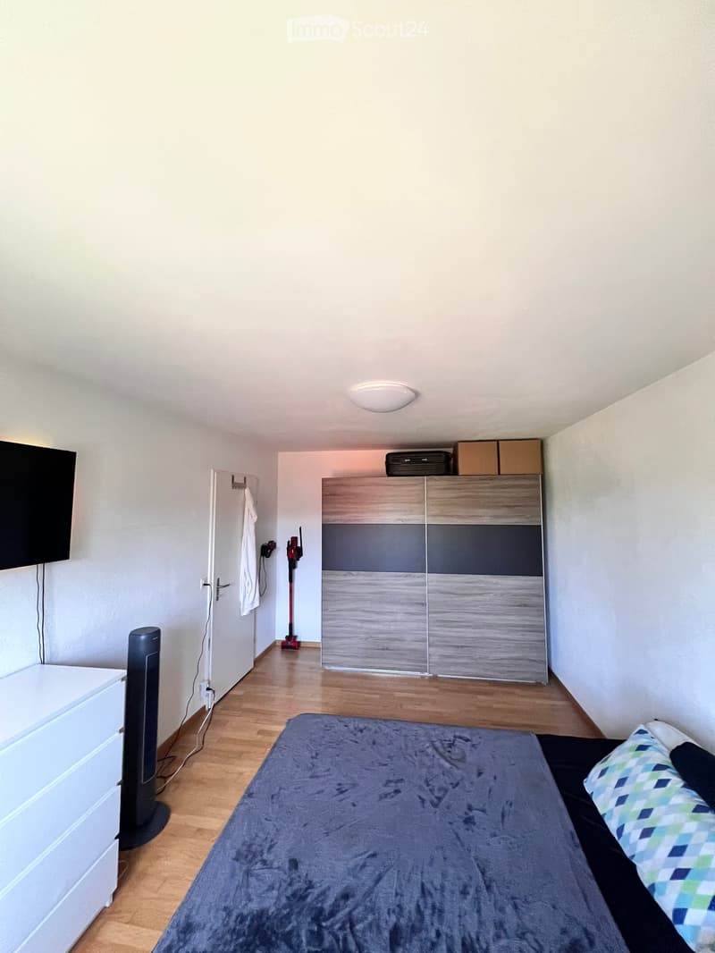A modern bedroom with a bed, pillows, a wardrobe, a fan, and a screen mounted on the wall.