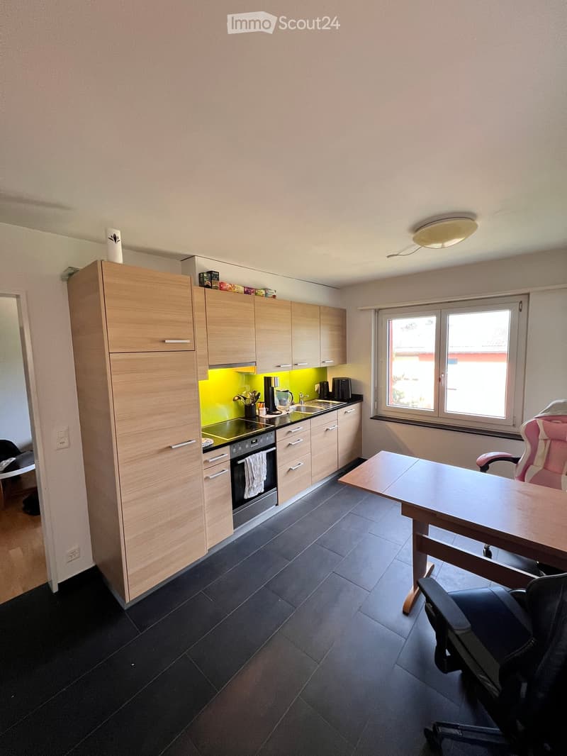 Modern kitchen with light wooden cabinets, black countertops, and a small workspace area with a table and chairs.