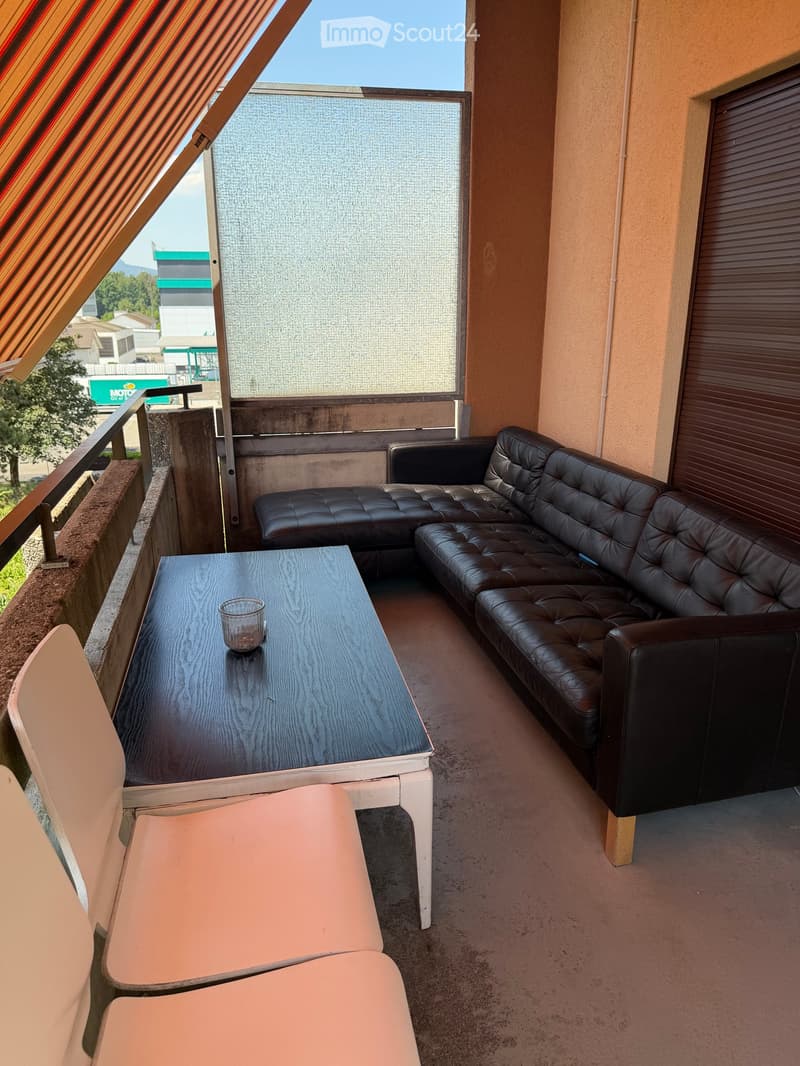 Balcony with a black leather sofa, a wooden table, and two white chairs. The balcony has a railing and a view of the street.
