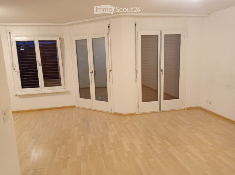 Empty room with light wooden flooring, white walls, and multiple large windows and sliding doors.
