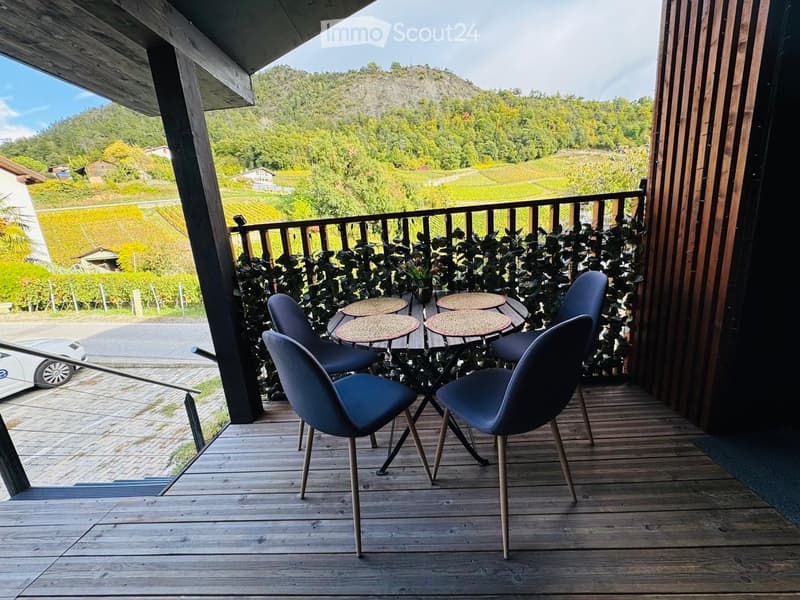 Wooden balcony with a scenic view of vineyards and hills, featuring a small table and four chairs.