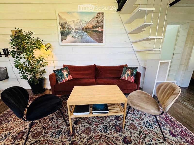 Living room with a red sofa, wooden coffee table, two chairs, a floor lamp, and a potted plant. A large picture frame hangs on the wall.