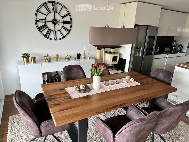 Modern dining area with a wooden table, four chairs, a vase with tulips, a cat tree, and a sleek kitchen area with stainless steel appliances.