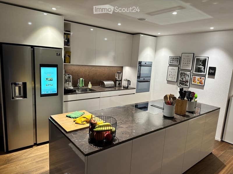 Modern kitchen with white cabinets, stainless steel appliances, granite countertop, and various kitchen items including a refrigerator, oven, sink, blender, toaster, cutting board, fruit basket, and wooden utensils.