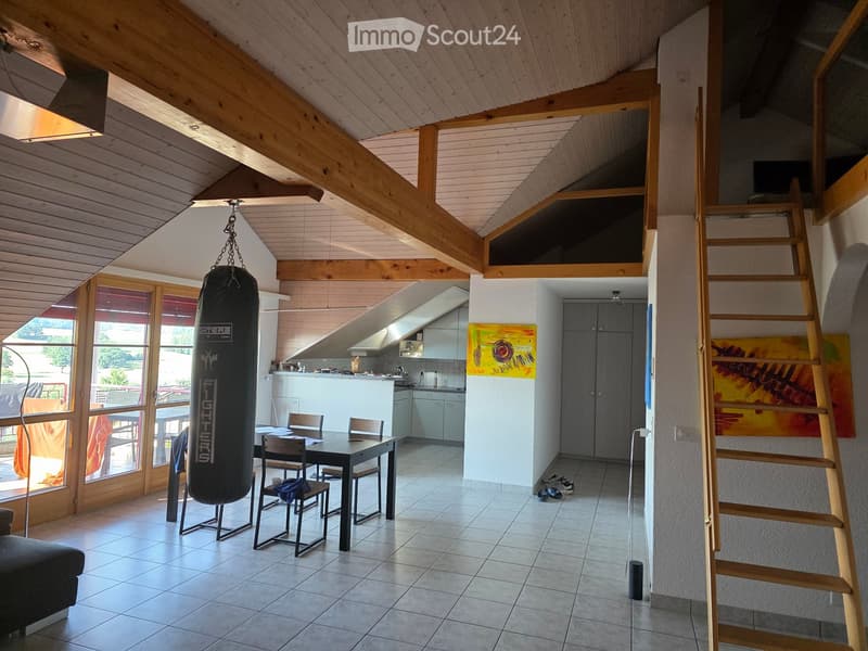 Open-plan living and dining area with exposed wooden beams, a dining table with chairs, a punching bag, a kitchen area, and a staircase leading to a loft space.