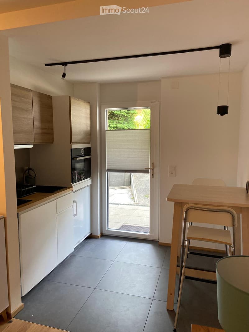 Modern kitchen with white cabinets, stainless steel appliances, and a small dining area with a table and chairs. A sliding glass door leads to a patio.