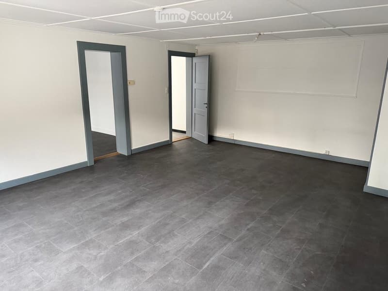 Empty room with grey tiled flooring, white walls, and two open doors leading to adjacent spaces.