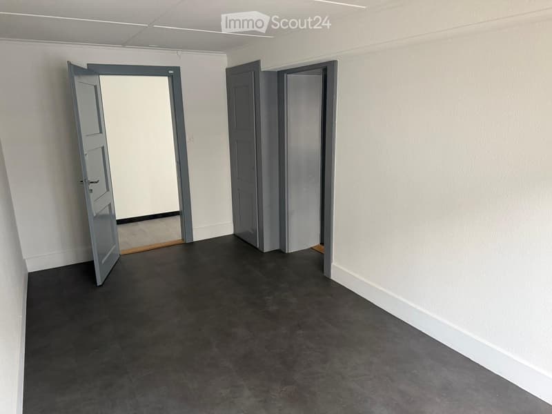 Empty hallway with grey doors, dark grey tiled floor, and white walls.