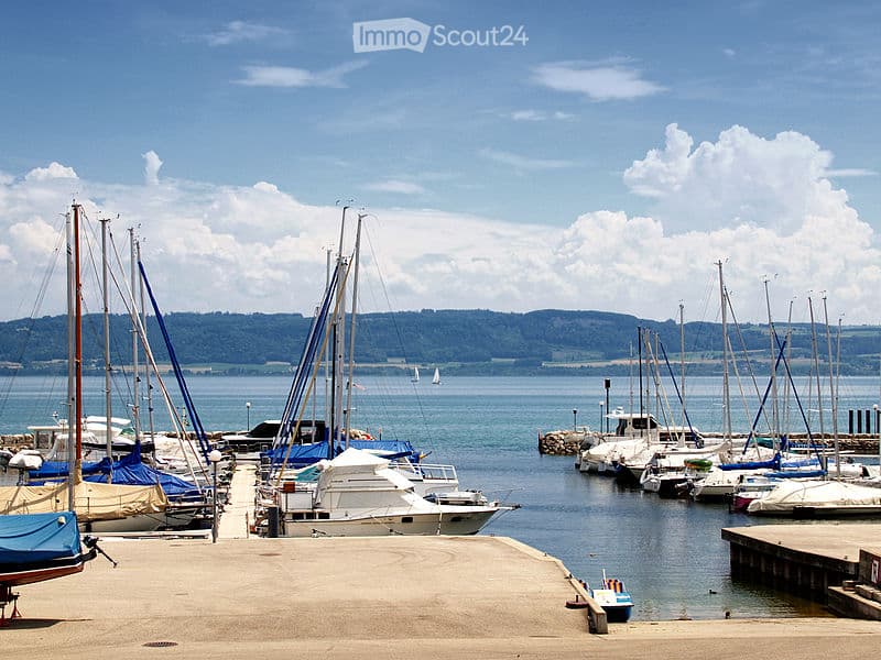 A marina with numerous sailboats and motorboats docked, surrounded by calm water and distant hills under a partly cloudy sky.