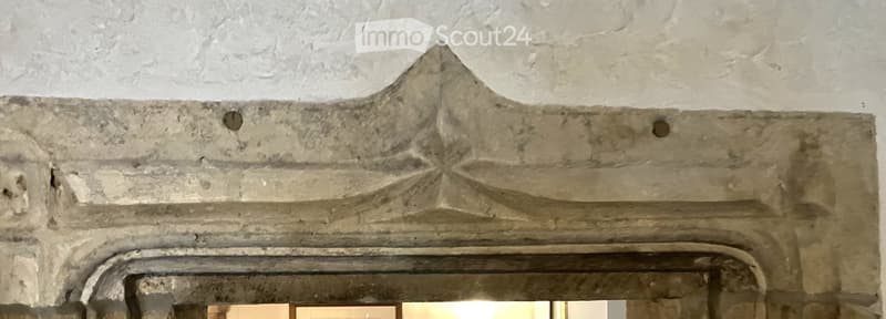 An ornate stone fireplace mantel with intricate carvings and a central star-shaped design, set against a textured white wall.