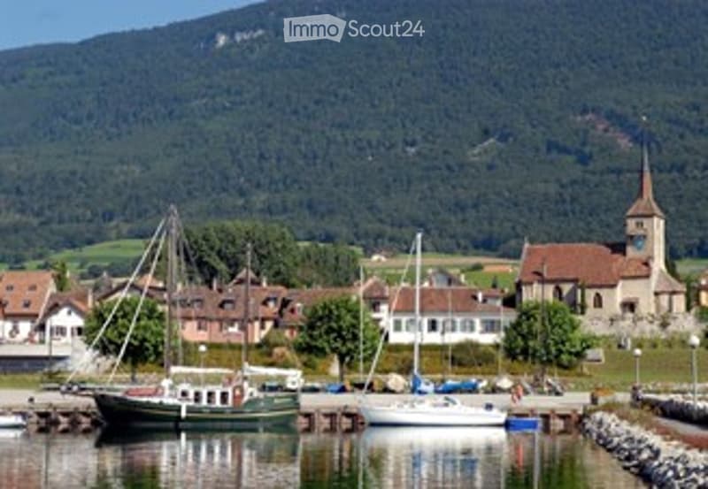 A picturesque harbor scene with several boats docked, surrounded by quaint houses and a church in the background, with a mountain range visible in the distance.