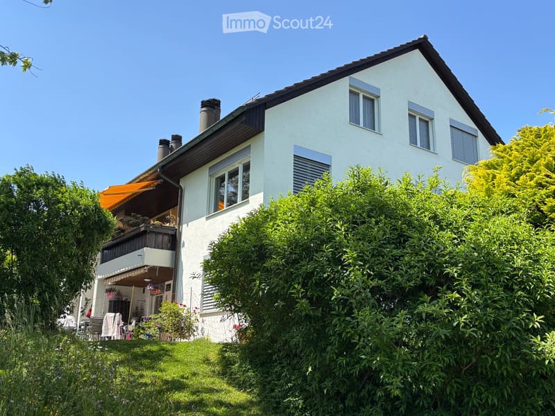 Two-story house with white exterior, multiple windows, and a balcony with outdoor furniture.